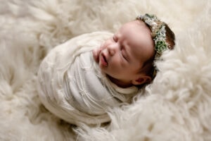 Newborn girl in the studio in Morgantown. She is wearing a white lace wrap and lying on a white fur.
