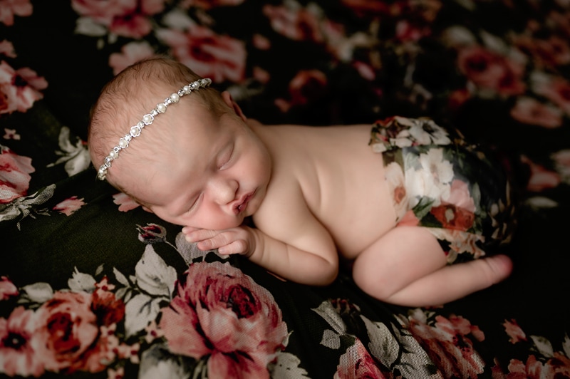 Newborn girl in the studio posed on a table with a flower background.