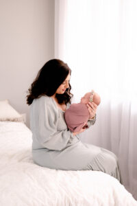 Mom sitting on the white bed, holding her newborn girl.