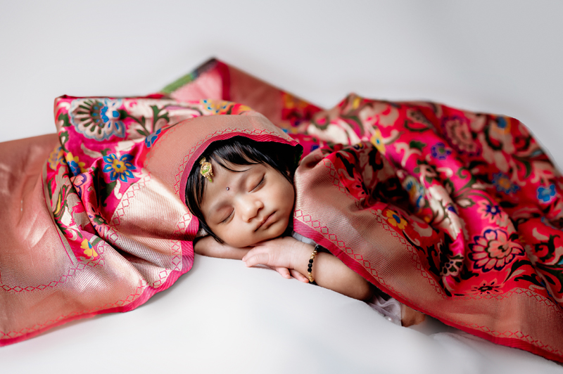 Newborn girl lying on a white backdrop with a ghoonghat covering.