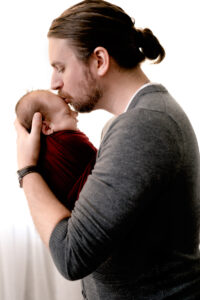 Dad holding newborn baby boy, giving him a kiss on the forehead.