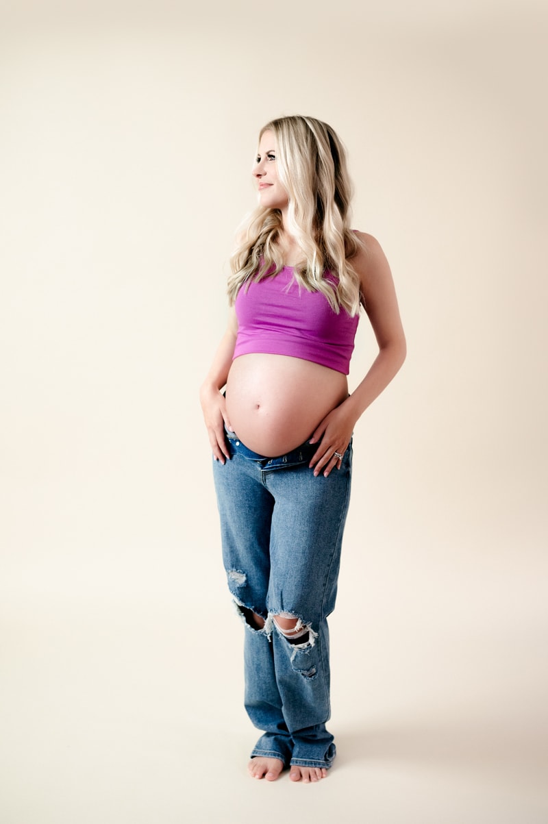 Expectant mom wearing a crop top and jeans in studio.