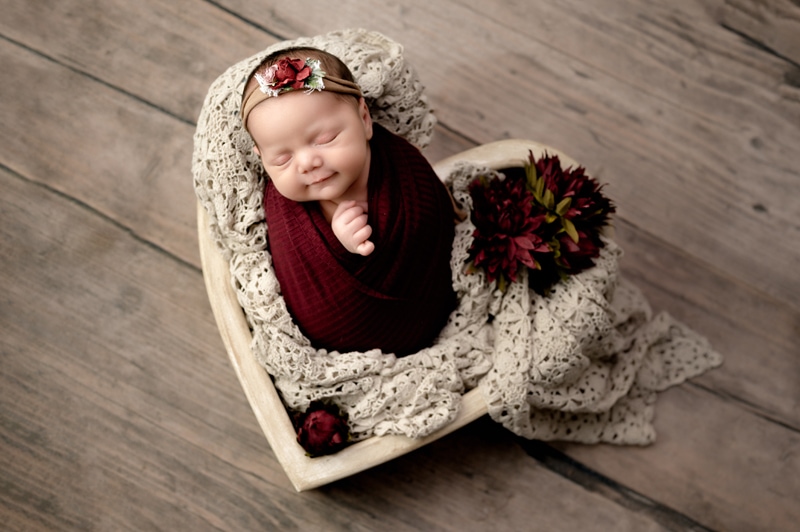 Newborn baby girl in a heart bowl with antique lace blanket and flowers.