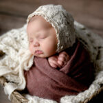 Newborn girl in a basket with a lace bonnet.
