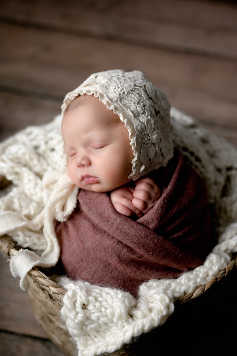 Newborn girl in a basket with a lace bonnet.