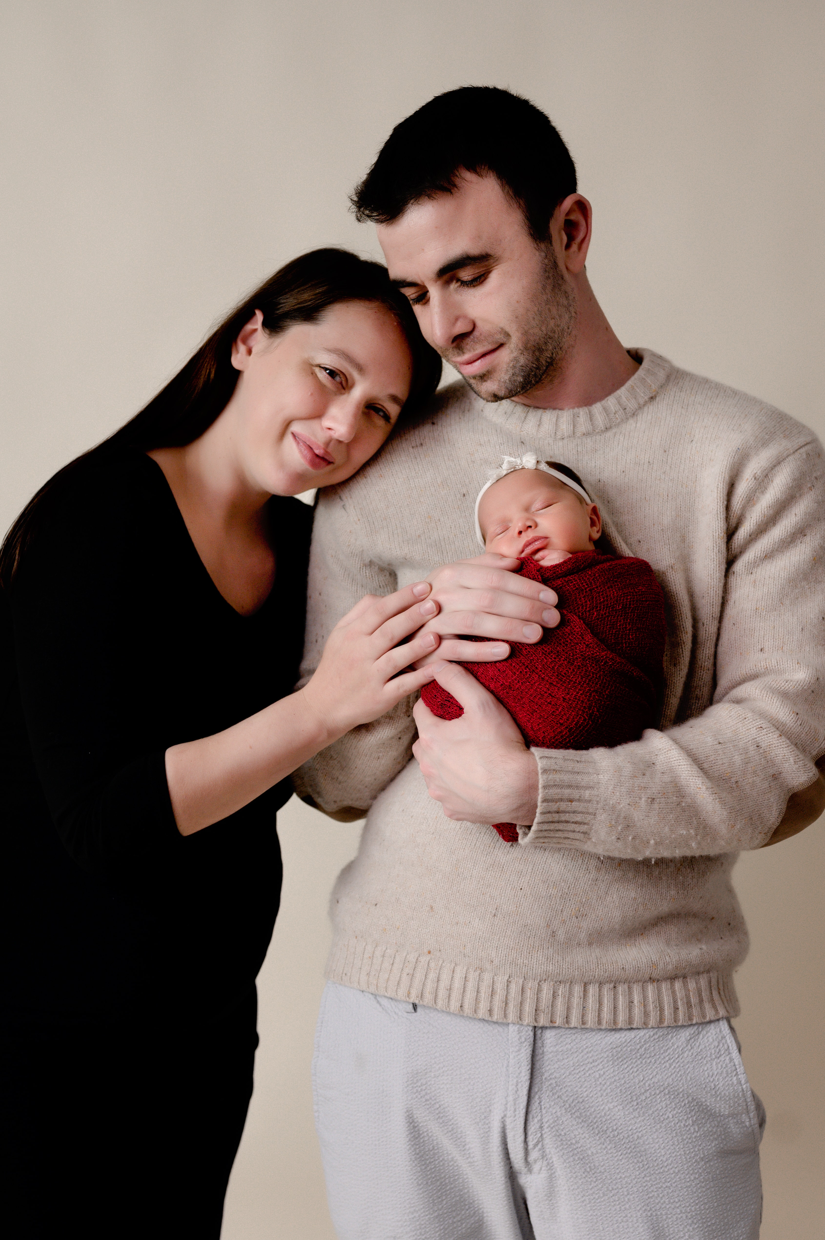 Family newborn photoshoot in studio. Dad is holding baby while mom and dad are cuddled up together.
