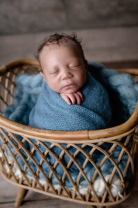 Newborn studio session with baby wrapped in blue, sitting in a basket.