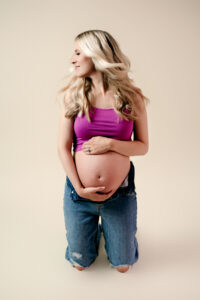 Maternity photoshoot in studio. Mom is wearing is a crop top and ripped jeans.