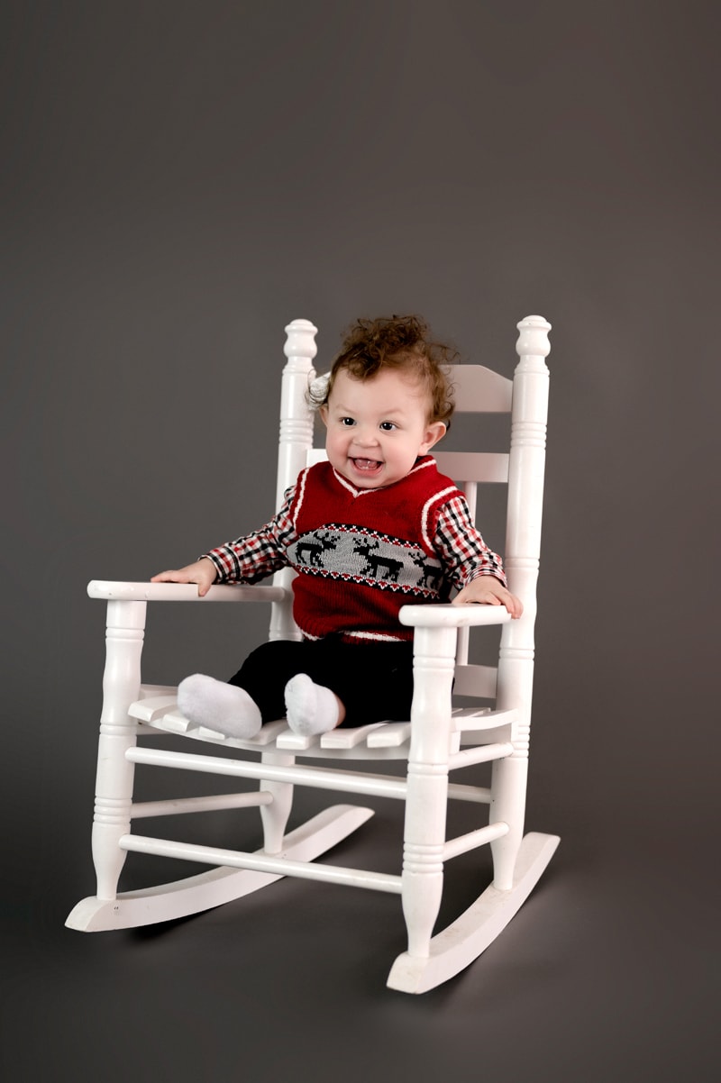 First birthday pictures in studio. Little boy in a cracker barrel rocking chair that's white on a gray background.