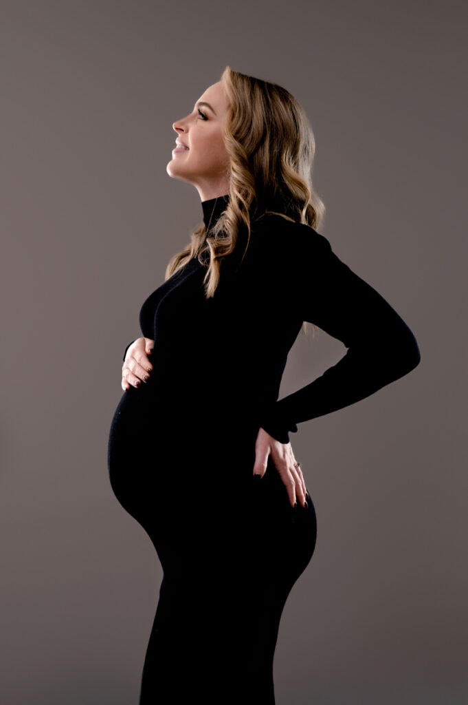 Mom to be in a black dress with a gray background. Studio maternity photoshoot.
