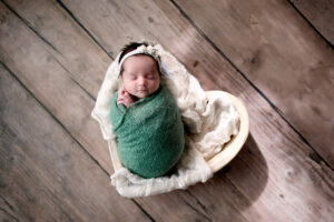 Newborn girl in a heart bowl with lace layer under her and a green wrap.