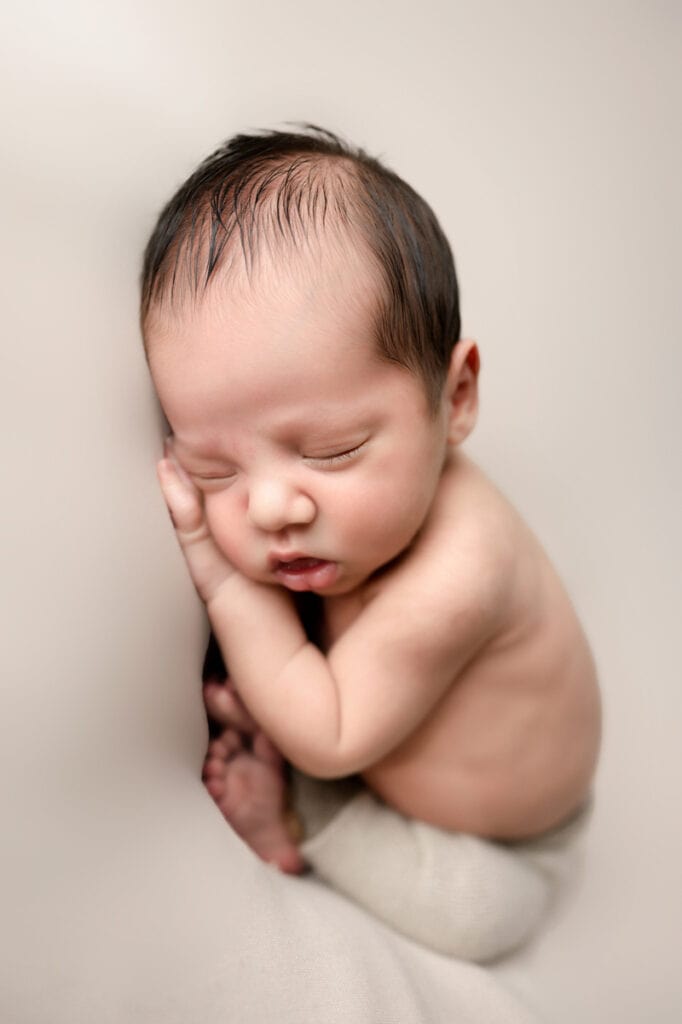 Newborn boy on a posing table in neutral colors.
