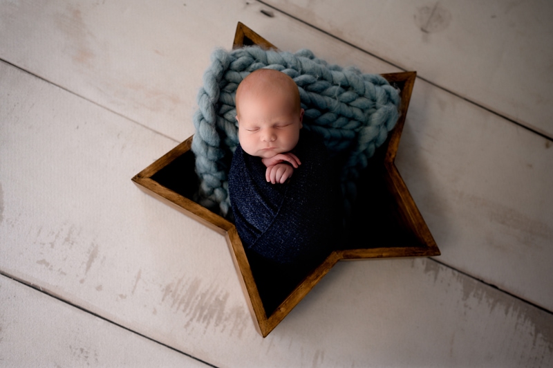 Newborn baby photoshoot in studio. Baby boy is posed in a star with the color blue.