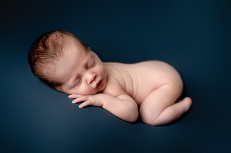 Newborn boy in studio. He is lying on a blue background with his hand under his cheek.