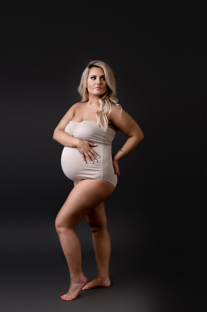 Maternity photoshoot in studio. Mom is wearing a white bodysuit with a dark gray background.
