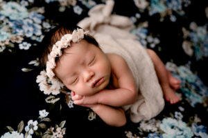 Morgantown, WV photographer with a newborn baby in the studio. Baby girl is posed on a navy floral backdrop and has on a beautiful cream colored bow headband.