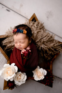 Morgantown, WV newborn photographer with another styled session in the studio. Newborn girl is wrapped in red, holding a red flower, and posed in a wooden star prop.
