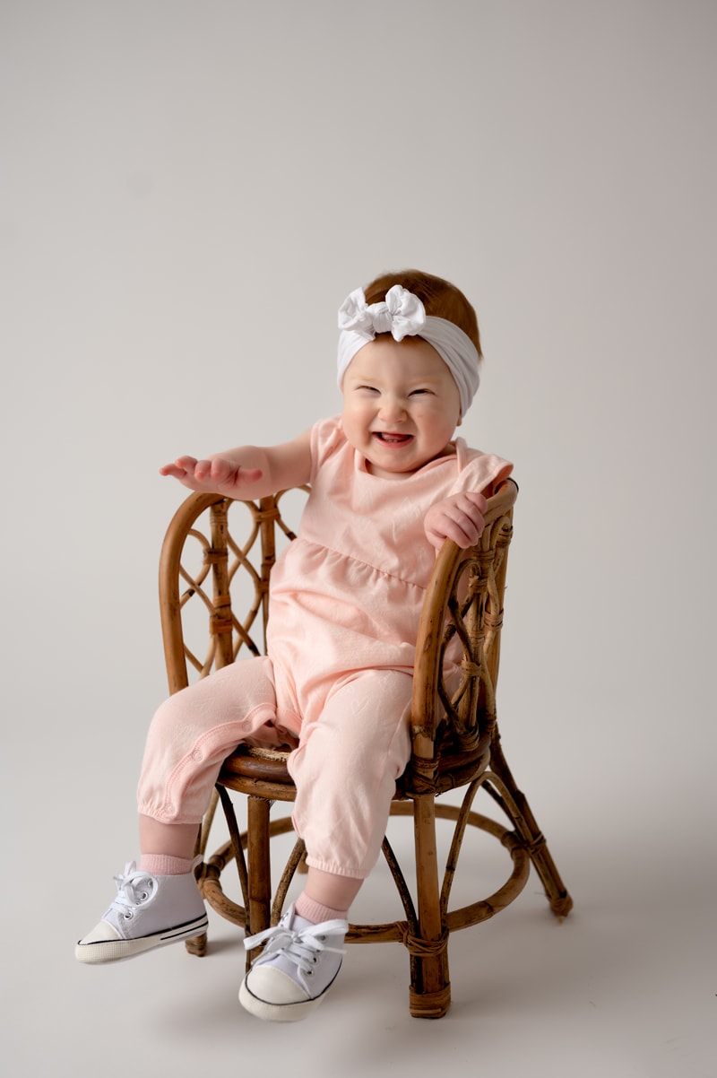 One year old session in the studio. She is sitting in a rattan chair and a white background.