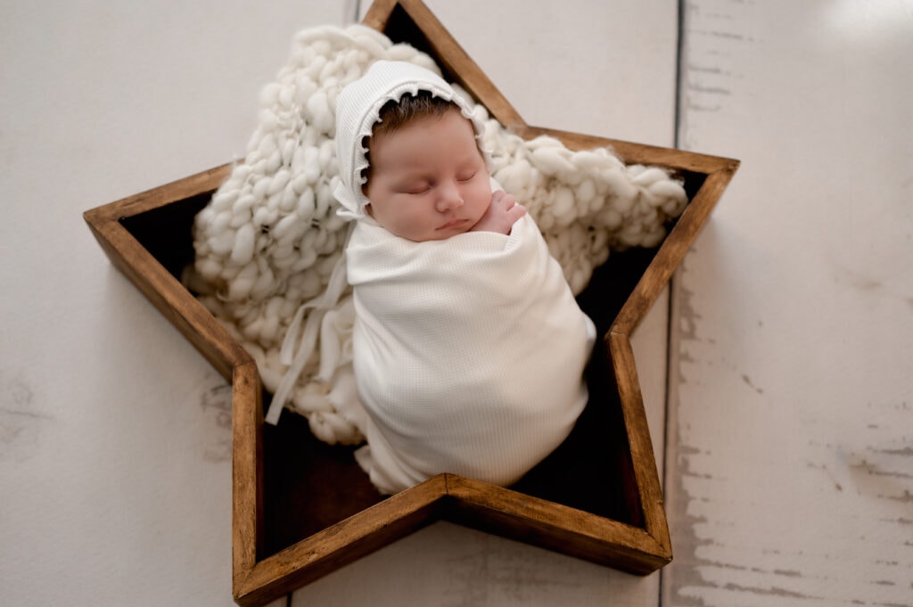 Newborn girl wrapped in cream and she is in a star prop.