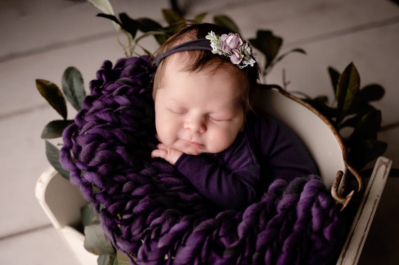 Newborn baby girl in purple and smiling.