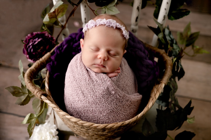 Newborn girl wearing purple in a basket.