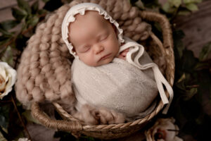 Newborn girl in a basket with a bonnet. Neutral colors.