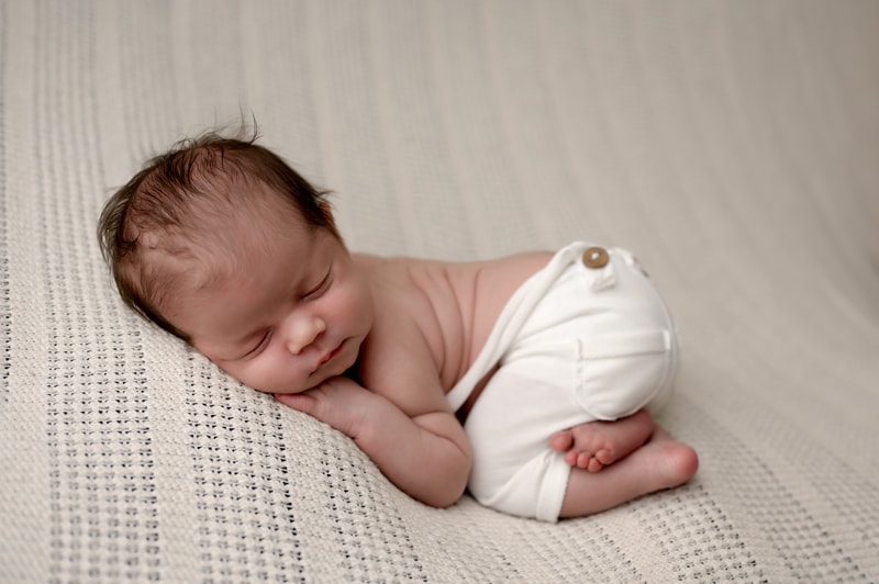 Newborn boy posed in pants on cream