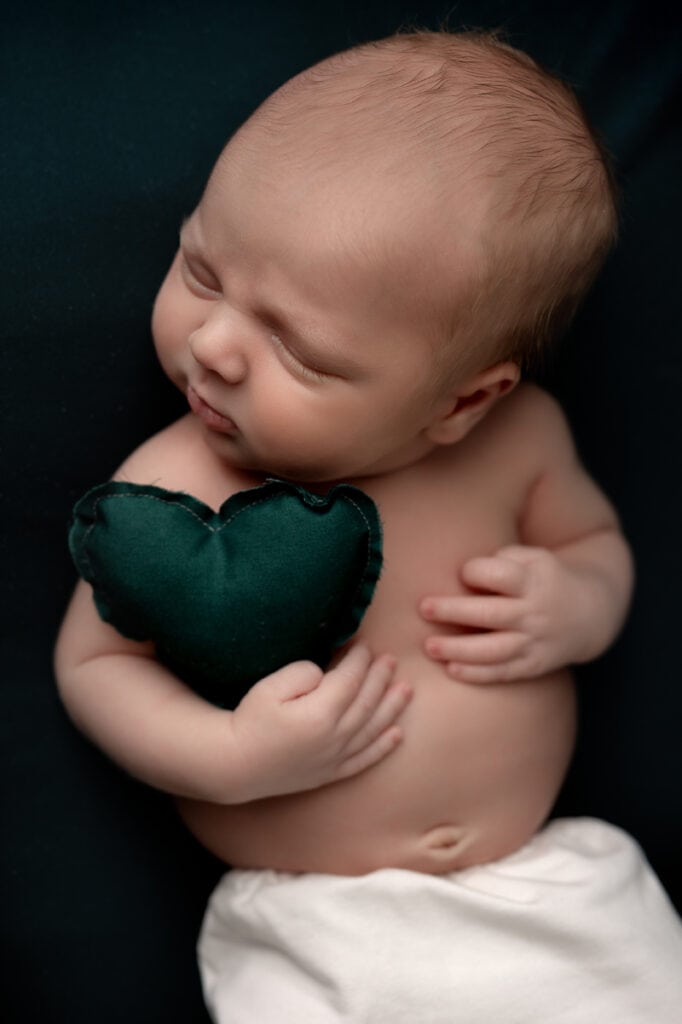 Newborn baby boy at his photoshoot, holding a heart.