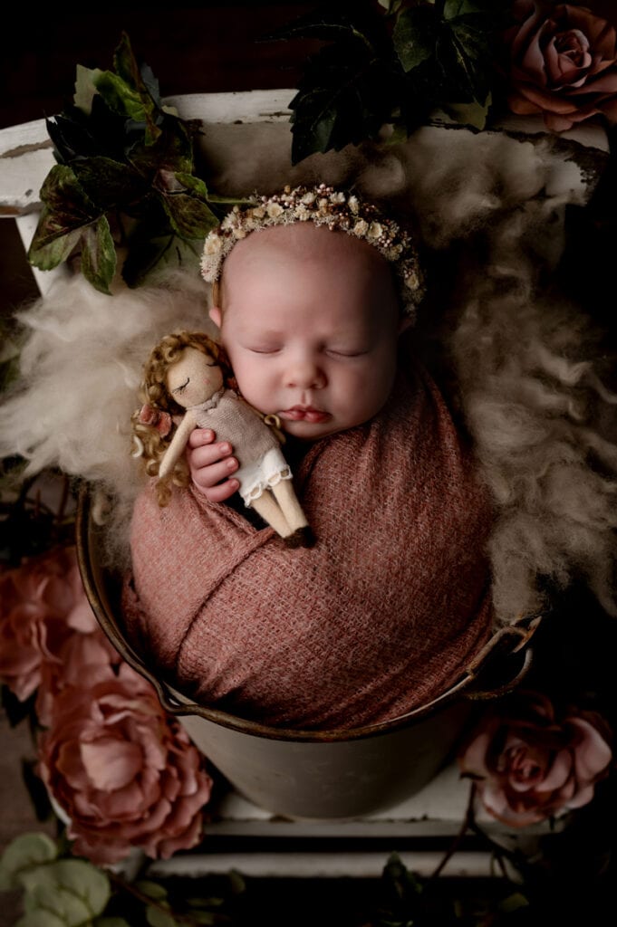 Newborn baby girl holding a baby doll with flowers.