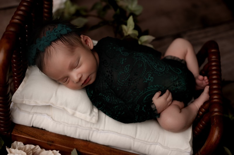 Newborn baby girl in a green lace outfit, on a bed.