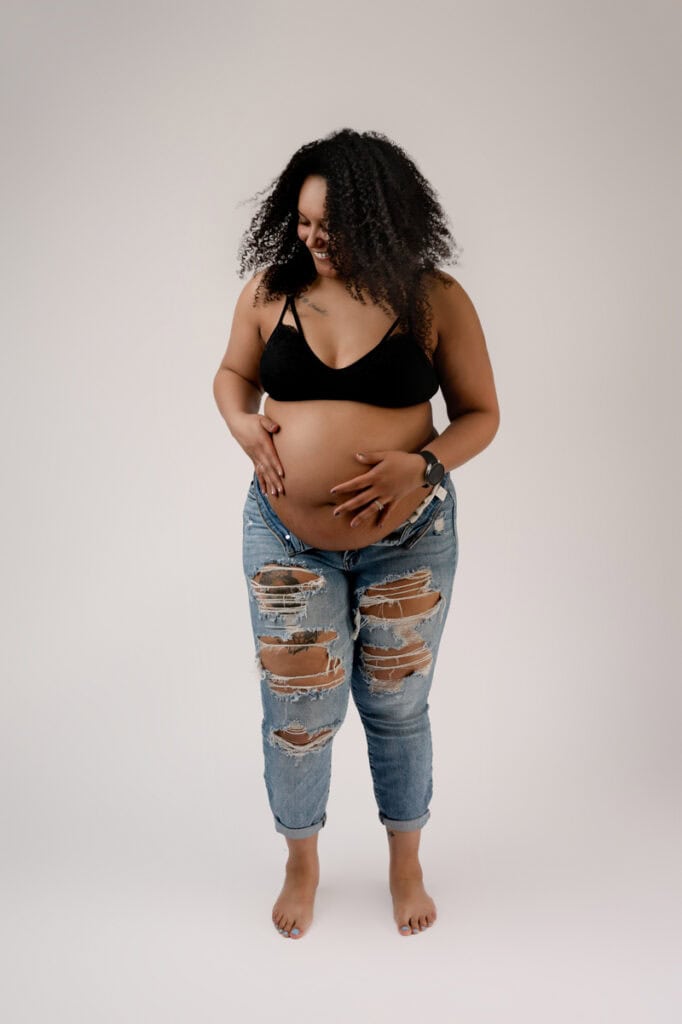Modern maternity in studio. Mom is wearing ripped jeans and a sports bra.