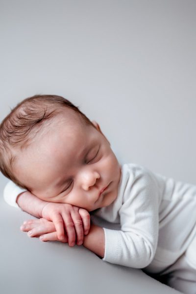 Newborn baby boy in studio wearing white with a white background.